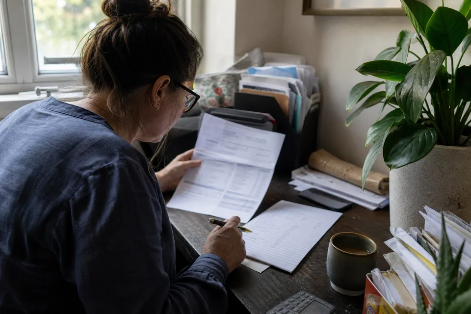 Renter comparing a bank statement with a handwritten list of rent reporting costs at a home desk