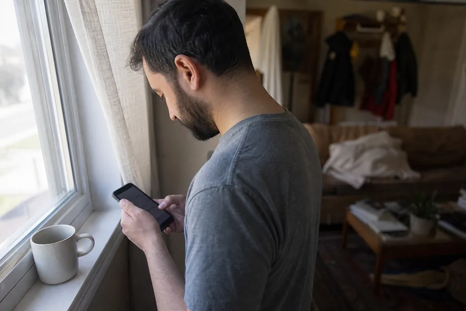 Renter paying rent on his phone by the window of a small rented home